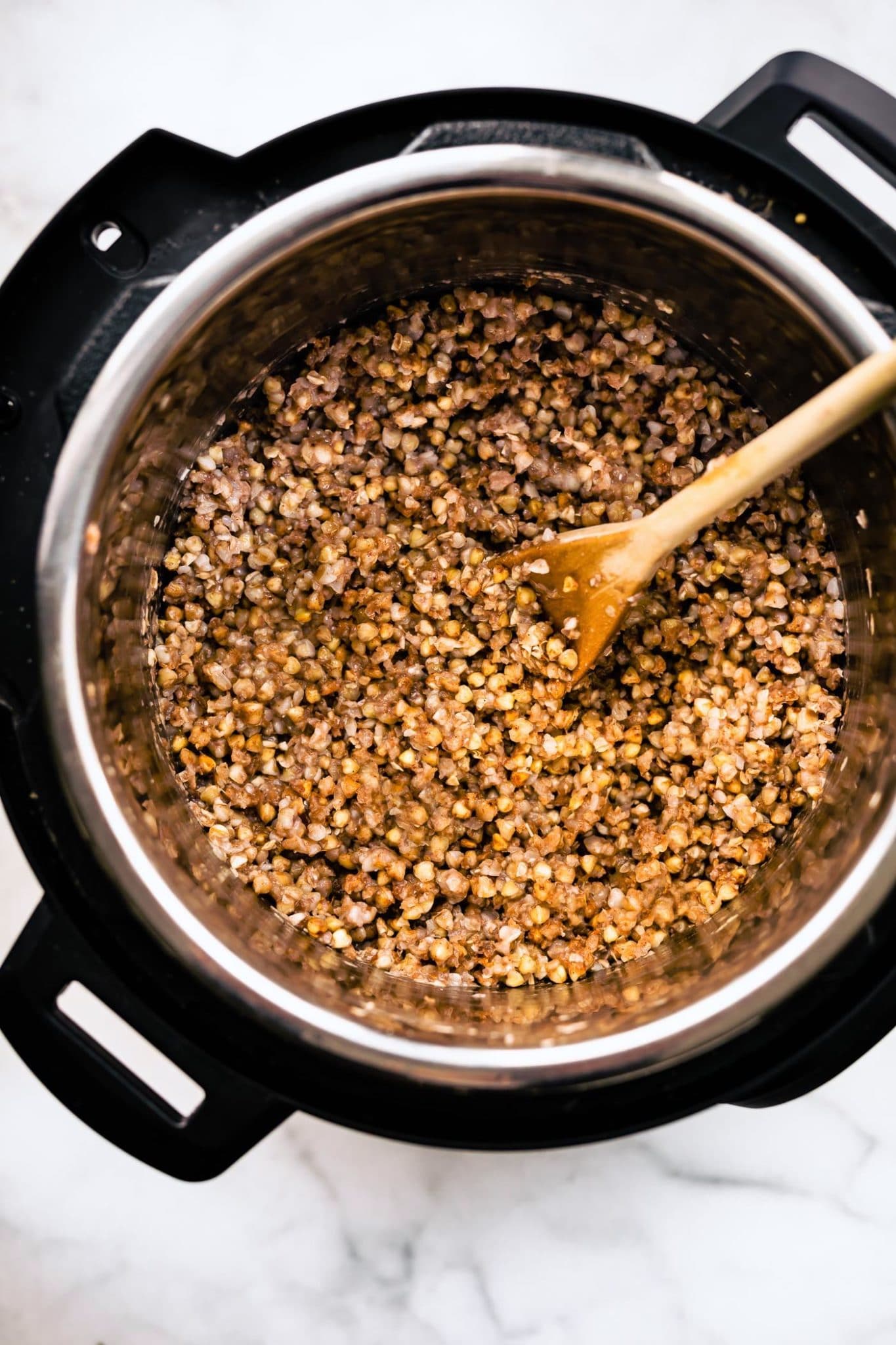 overhead image of cooked buckwheat in an instant pot being stirred with a wooden spoon