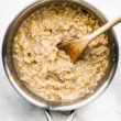 a sauce pot full of cooked rolled oats with spoon in middle