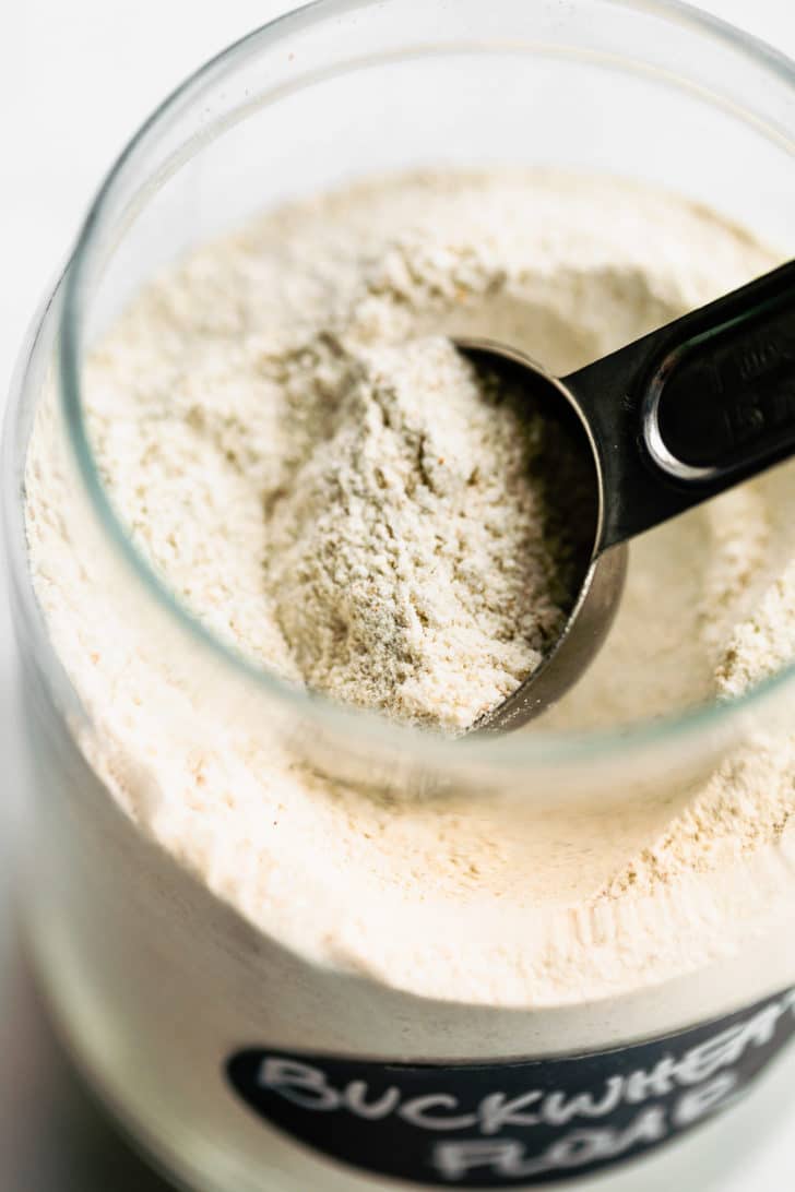 a glass jar full of buckwheat flour with a tablespoon scooping out a portion