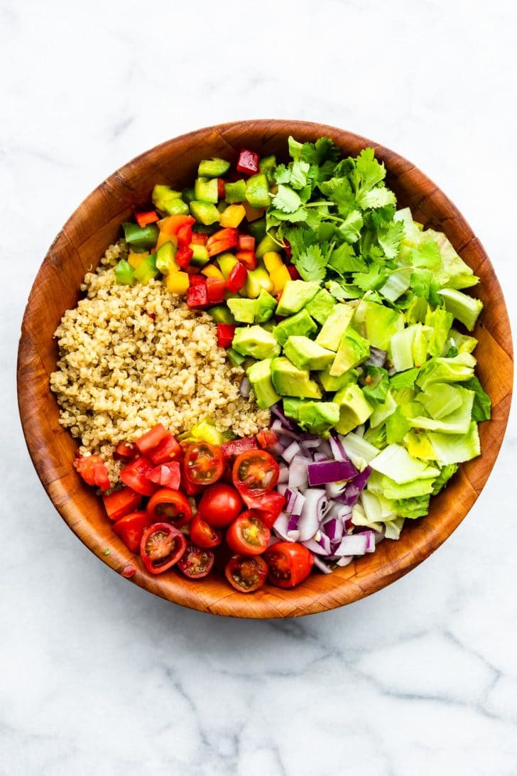 ingredients of Fiesta Quinoa Salad in wooden bowl. quinoa, peppers, cilantro, avocado, lettuce tomatoes