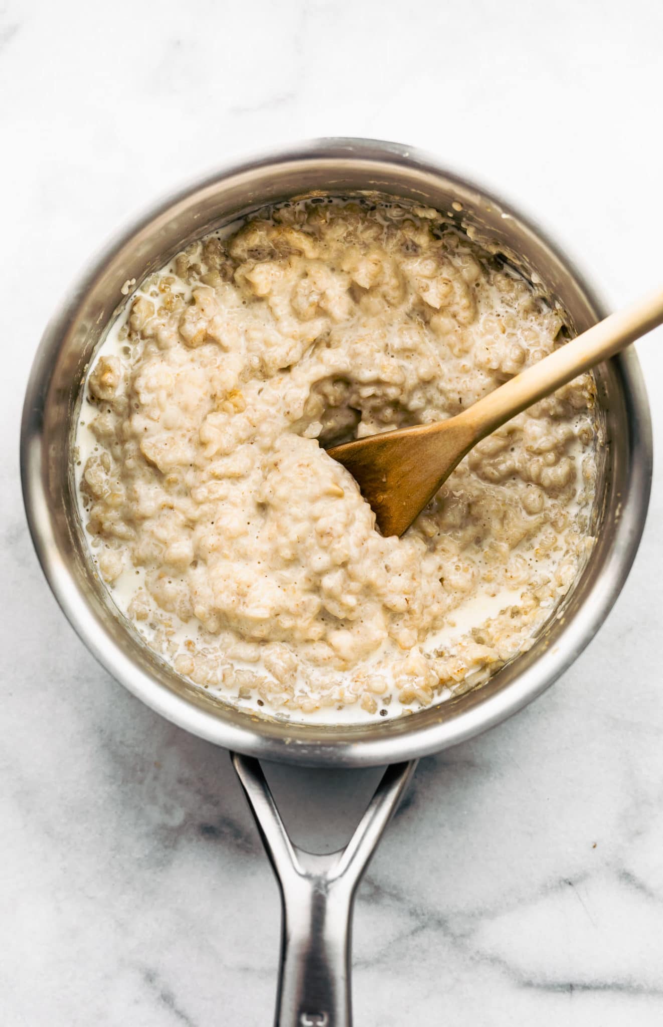 a sauce pot full of cooked quick oats in milk with spoon in middle