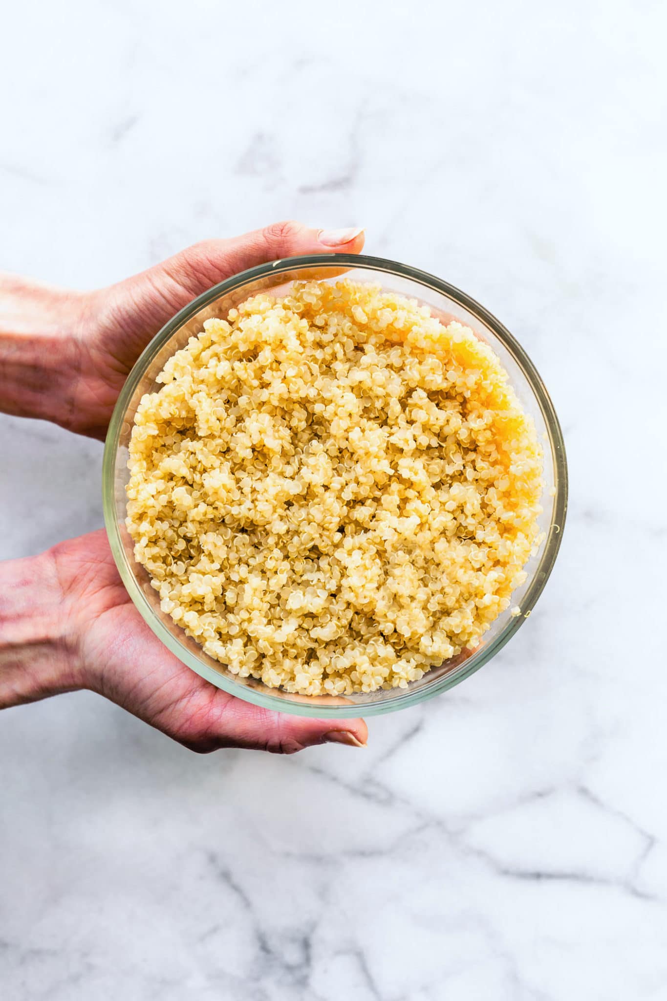 two hands holding a glass bowl full of gluten free quinoa grains