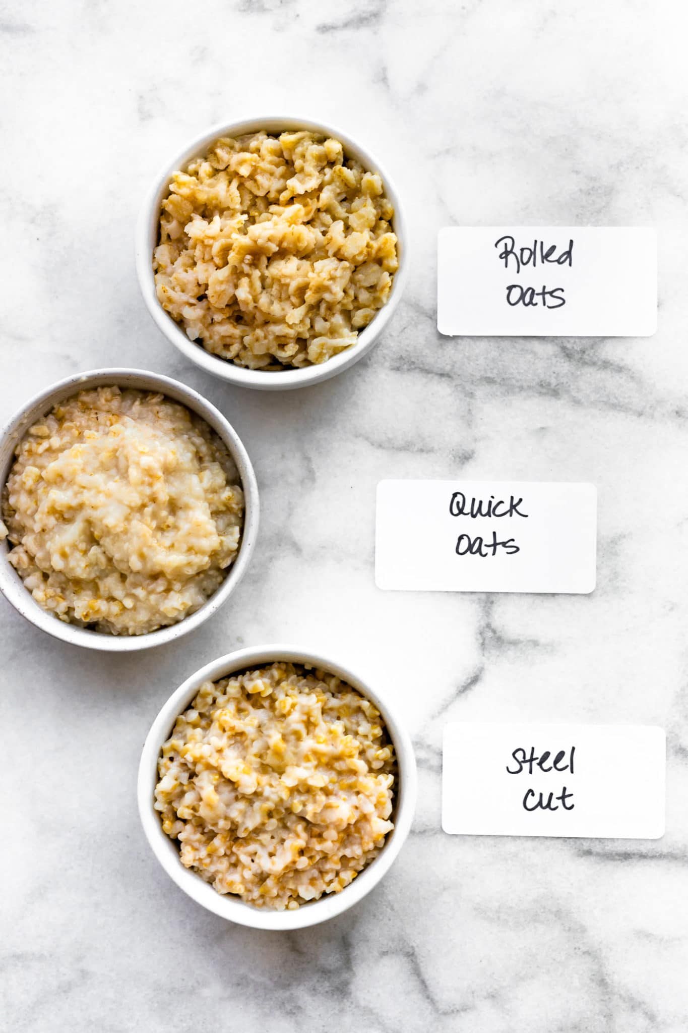 overhead image of cooked oats in white bowls labeled rolled oats, quick oats, and steel cut