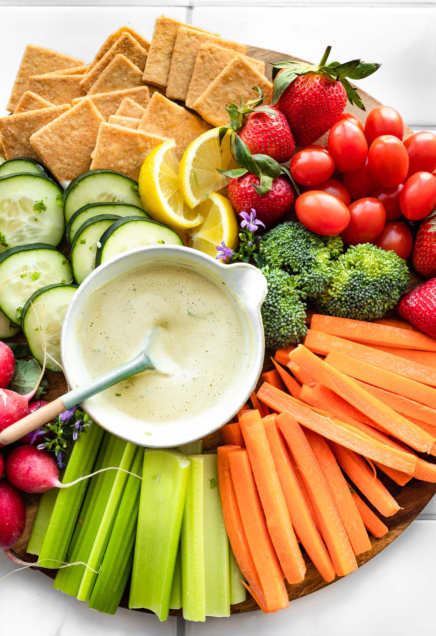a snack platter with celery sticks, carrot sticks, broccoli, strawberries, grape tomatoes, gluten free crackers, lemon wedges, cucumber sliced, radishes, and a bowl of homemade vegan ranch recipe in the center