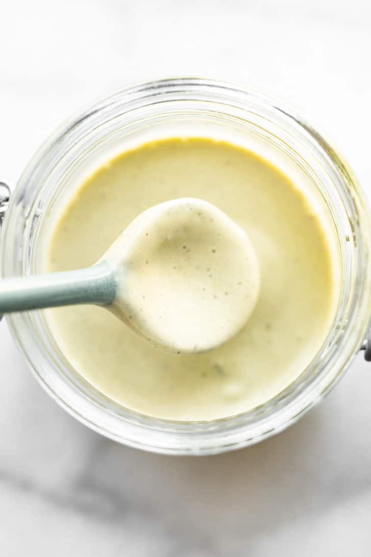 overhead image of homemade vegan ranch dressing in a clear jar being dipped with a spoon