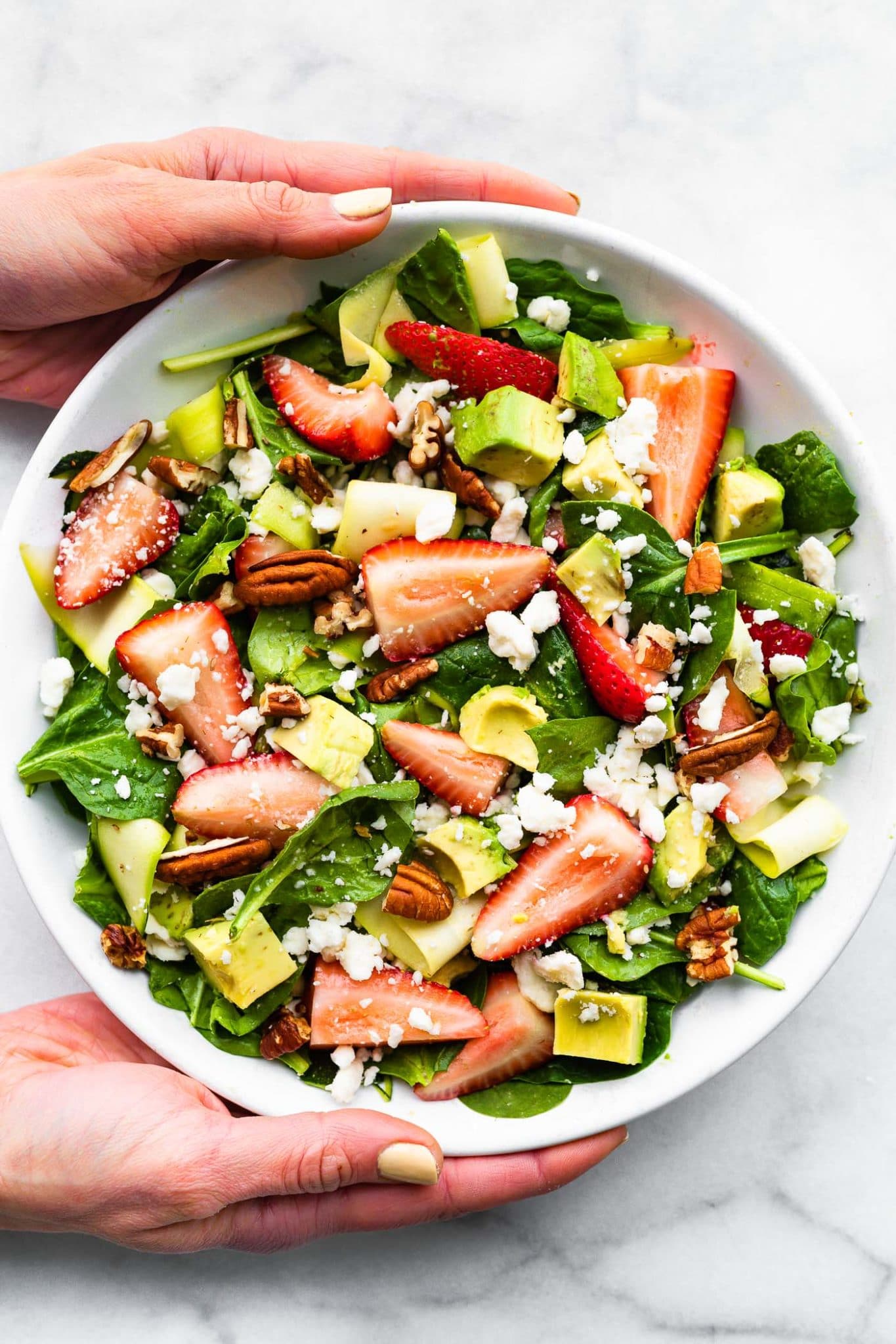 two hands holding a white bowl full of the best summer strawberry salad recipe