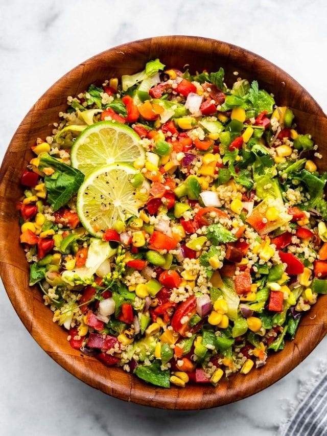 Wooden serving bowl filled with Fiesta quinoa salad with roasted corn and lime slices.