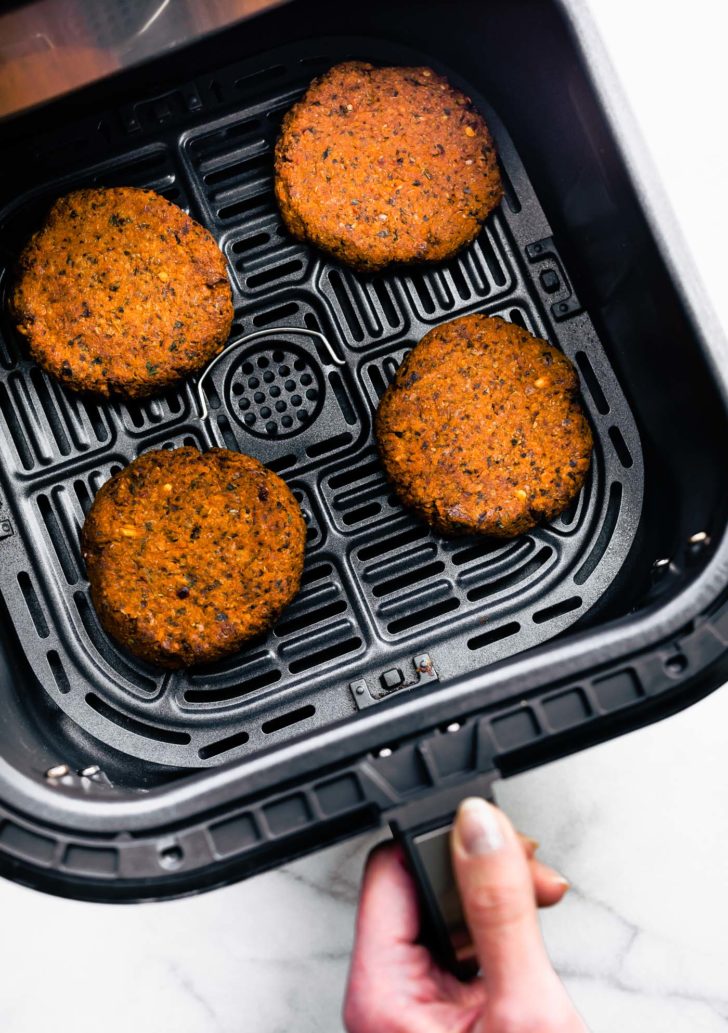 four vegan greek quinoa burger patties in an air fryer basket