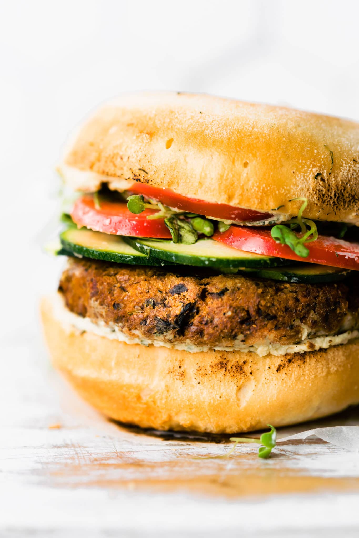 a vegan greek quinoa burger on a gluten free bun with tzatziki, cucumbers, tomatoes, and fresh herbs