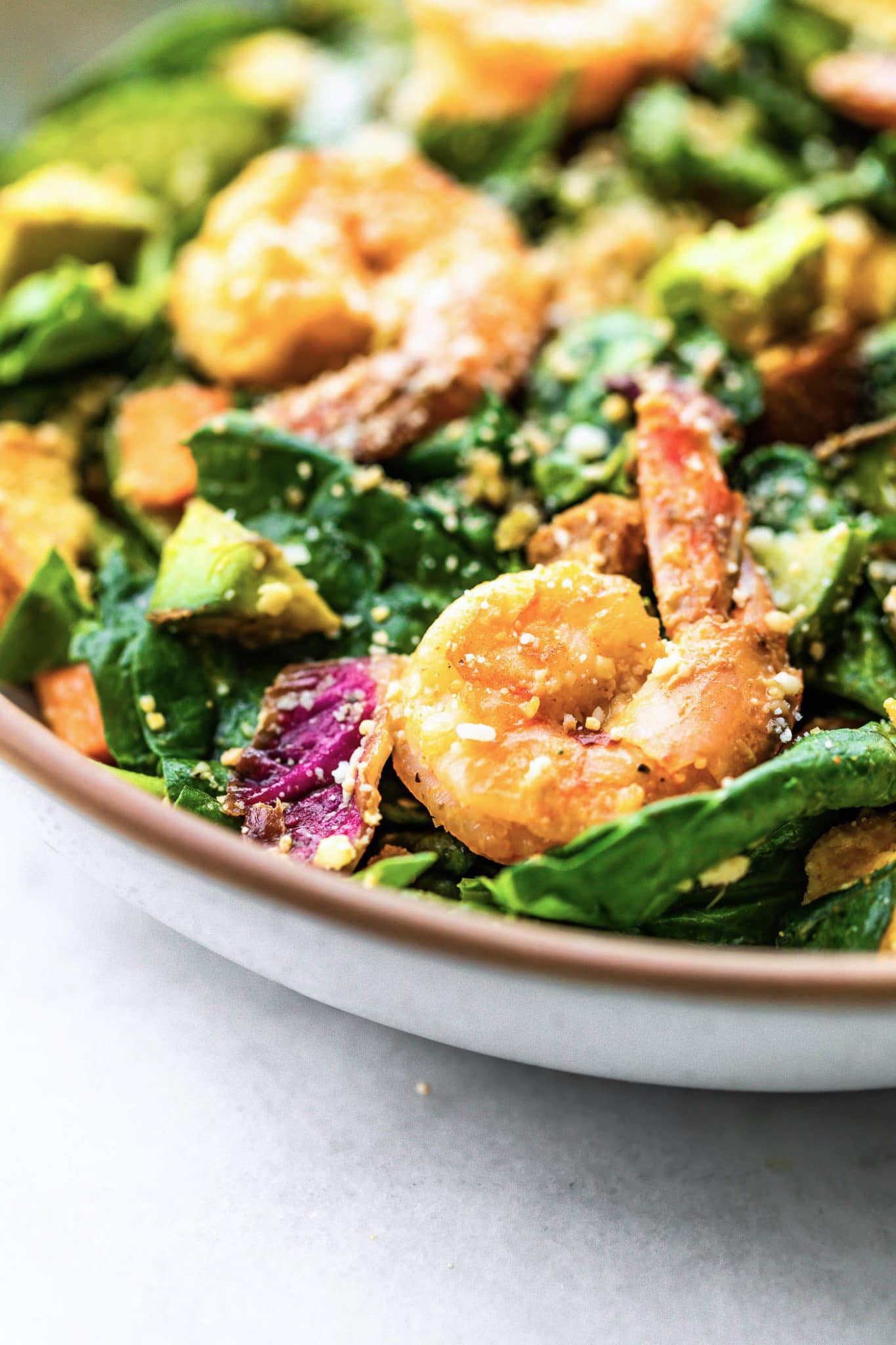 Close up view of spicy shrimp caesar salad in white bowl.