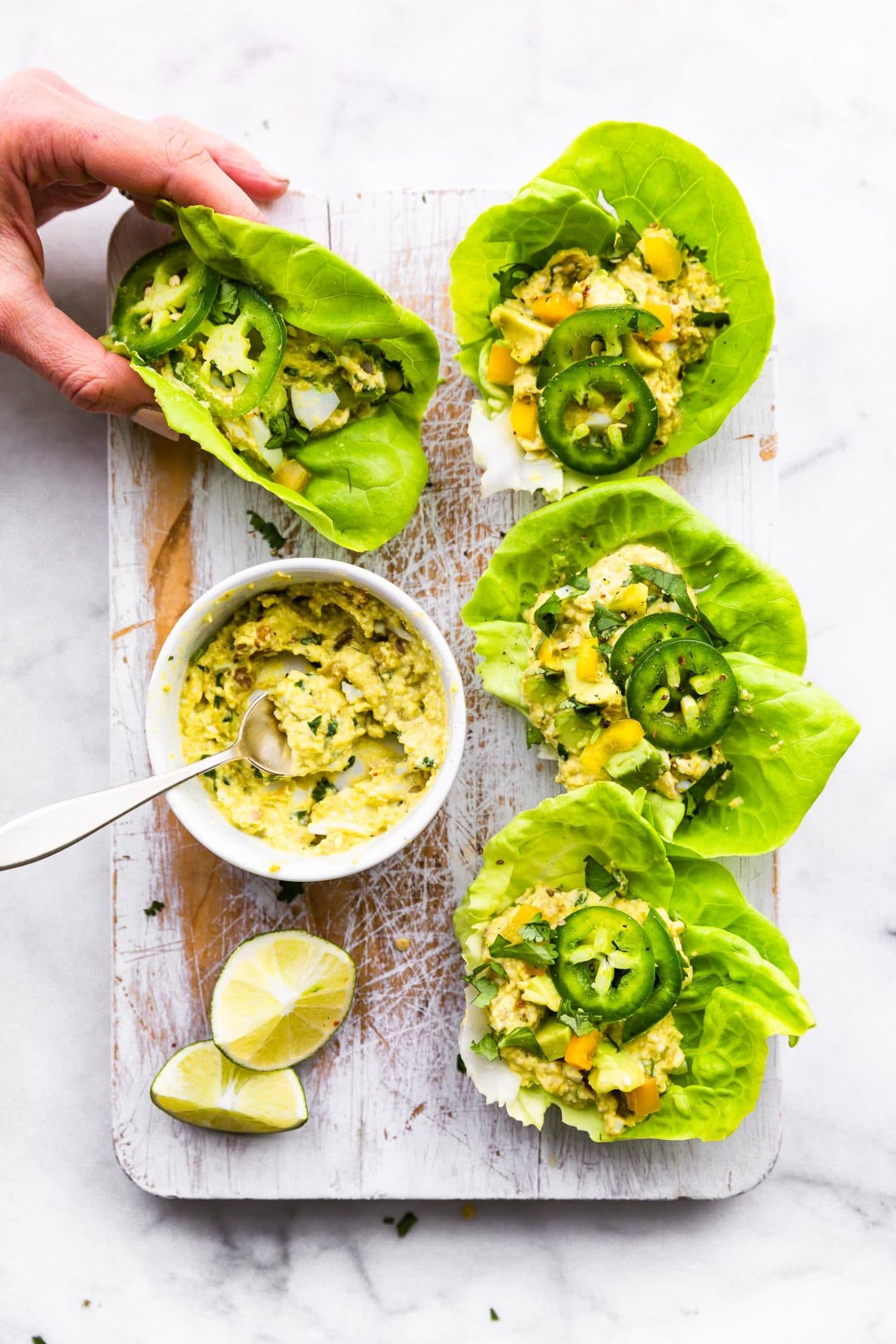 Mexican avocado egg salad in a bowl being spooned into 4 lettuce wraps and topped with jalapenos