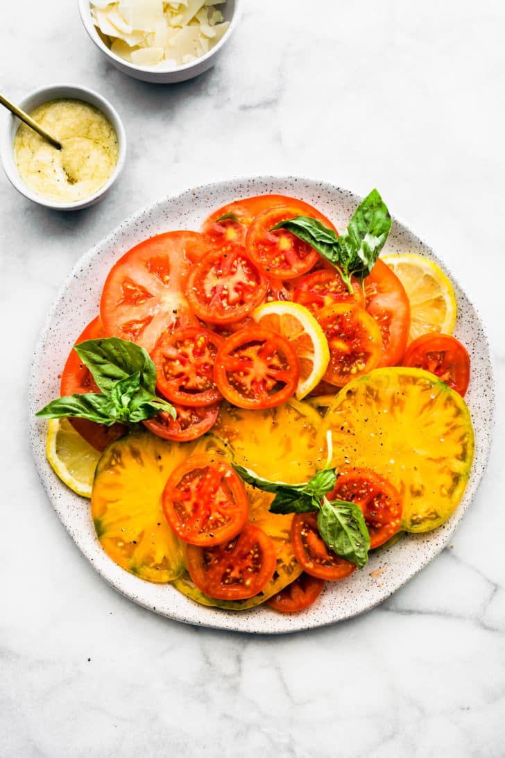 a white speckled plate with sliced cherry and heirloom tomatoes topped with fresh herbs