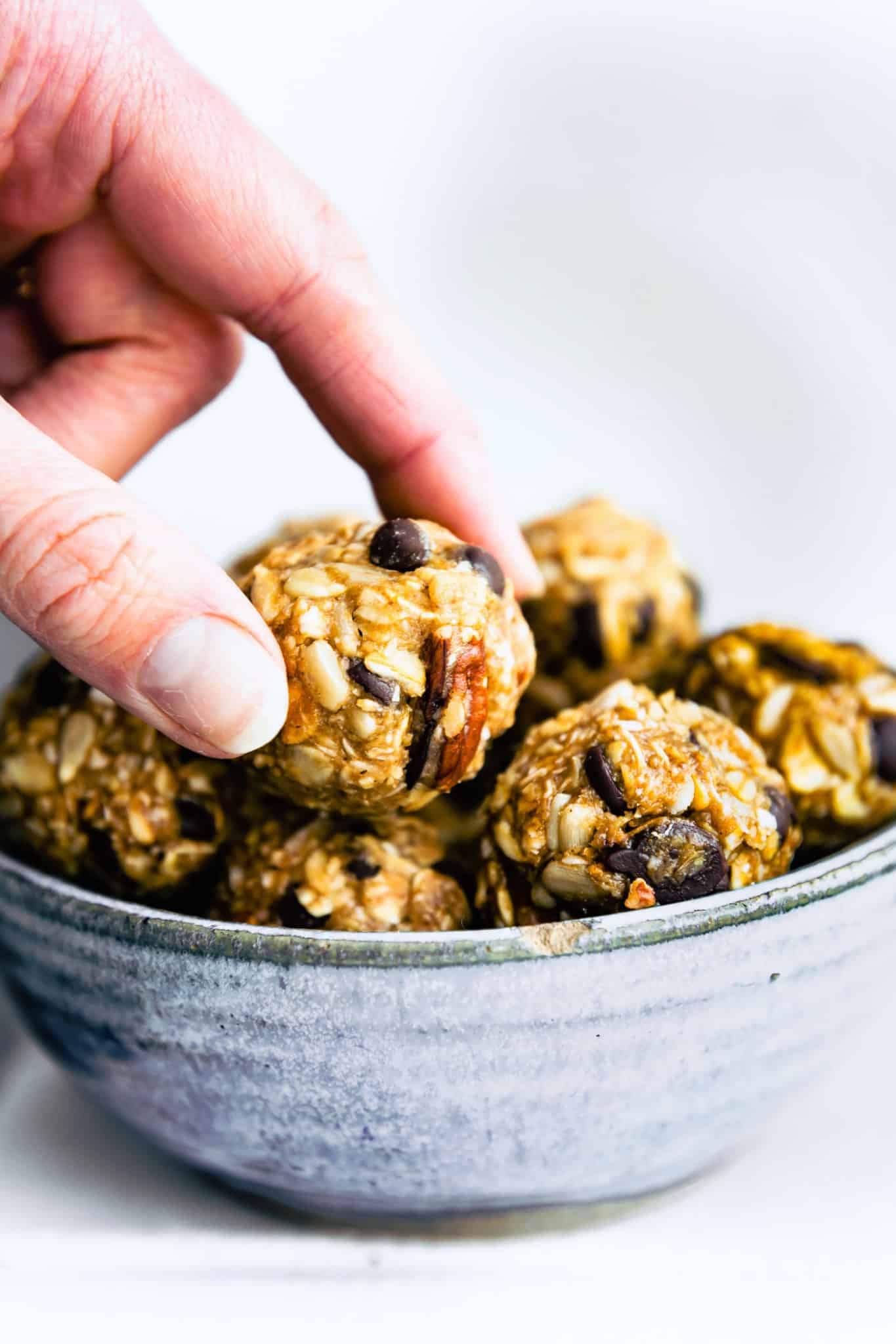 a hand grabbing a no bake cowboy cookie energy bite out of a bowl full of energy bites