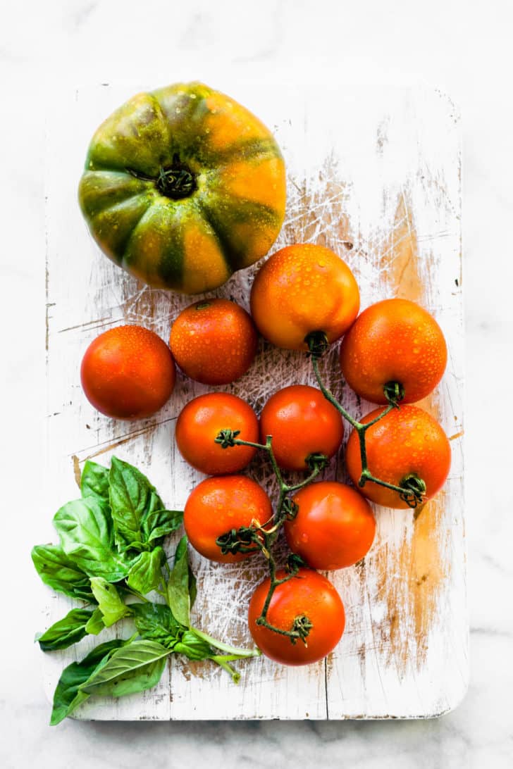 a cutting board with fresh herbs, on-the-vine tomatoes, and a large tomato