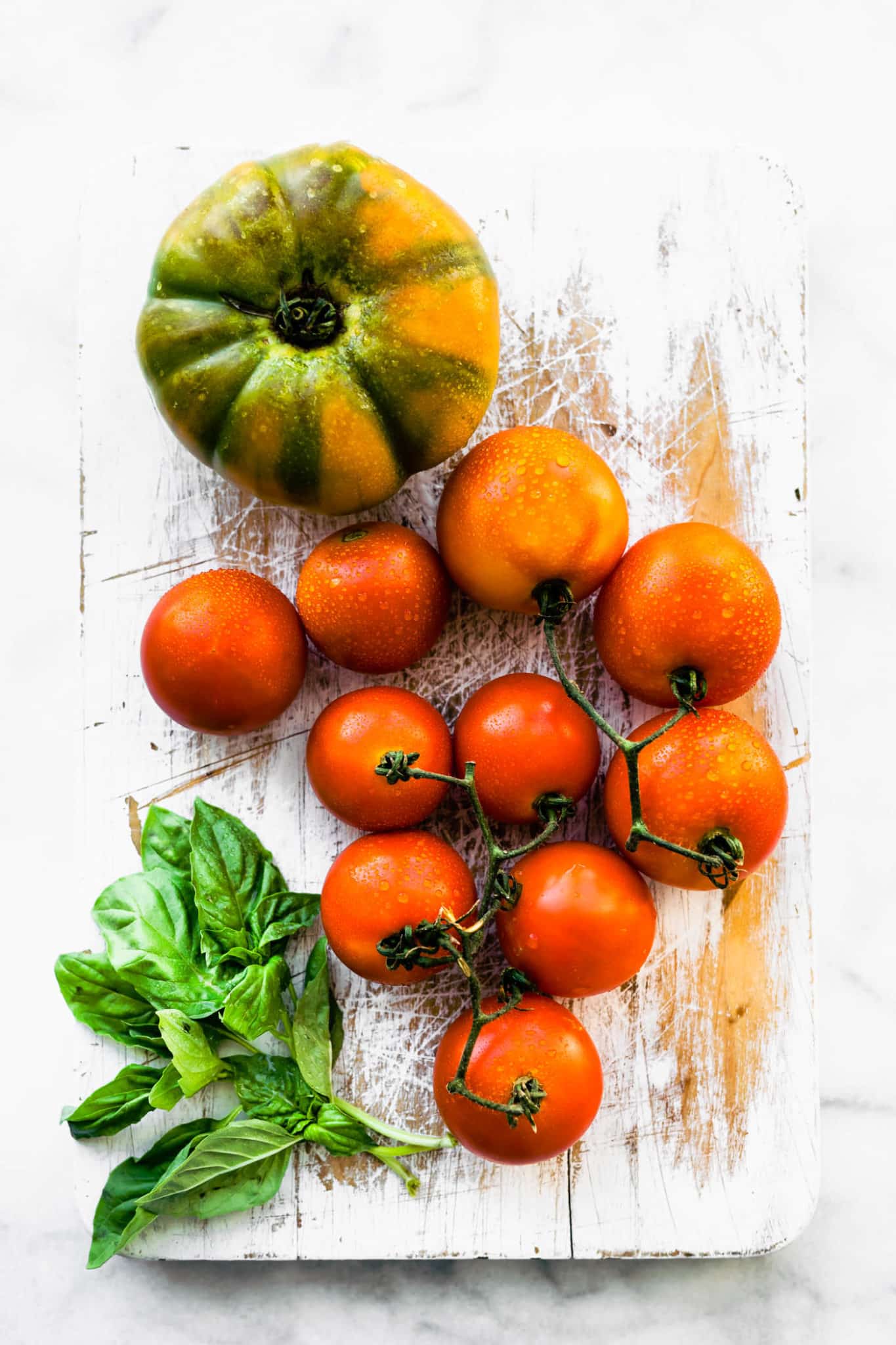 a cutting board with fresh herbs, on-the-vine tomatoes, and a large tomato.