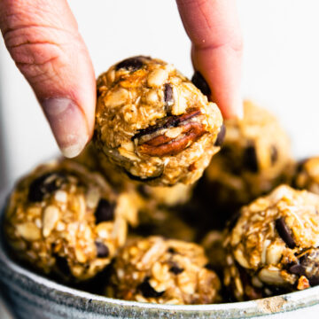 a bowl full of no bake cowboy cookie energy bites and a woman hands grabbing a bite