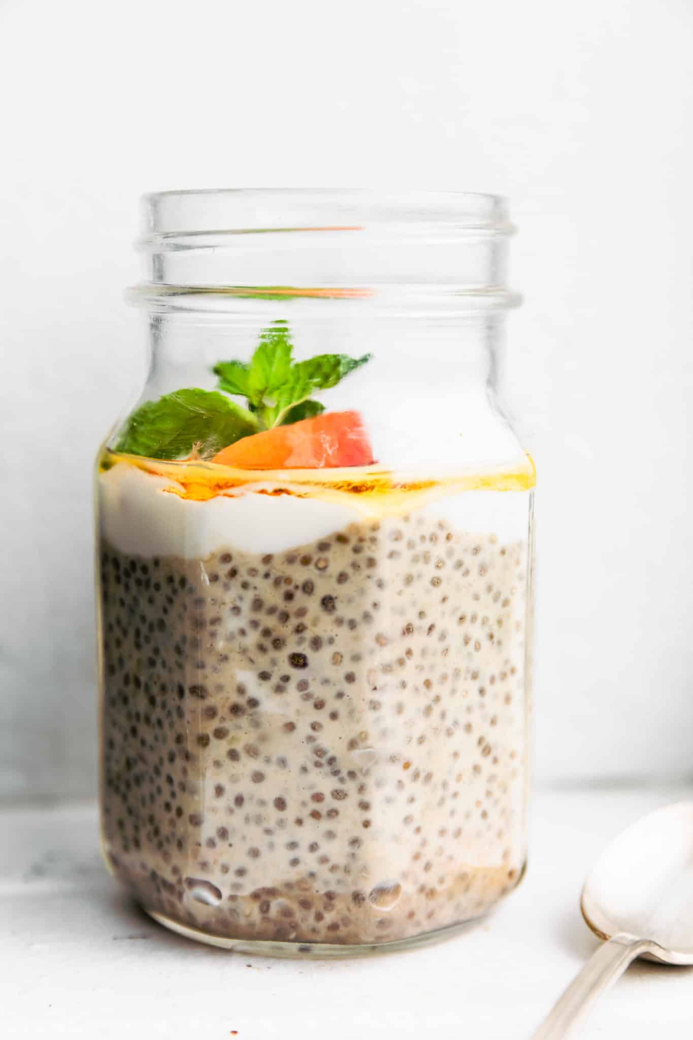 a jar of chia pudding with protein with layers of dairy-free yogurt, honey, peaches, and fresh mint on top