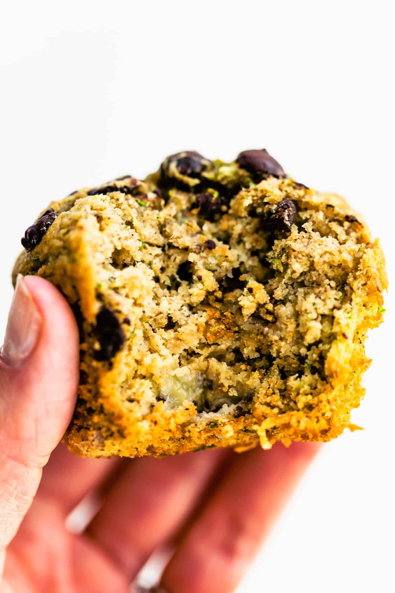 a woman's hand holding a chocolate chip gluten free zucchini muffin with a bite taken out
