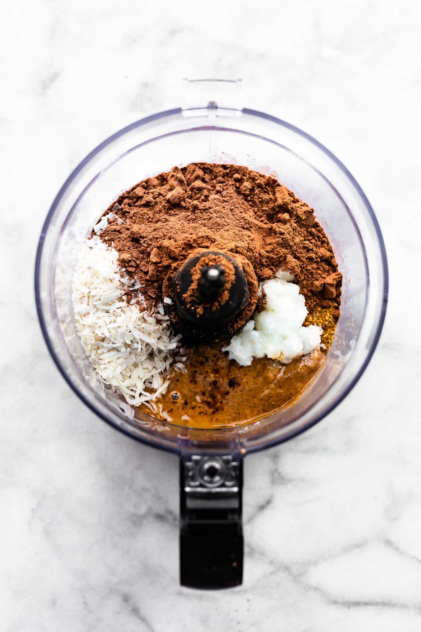 Overhead image of ingredients in a food processor. Cocoa powder, coconut, and nut butter.