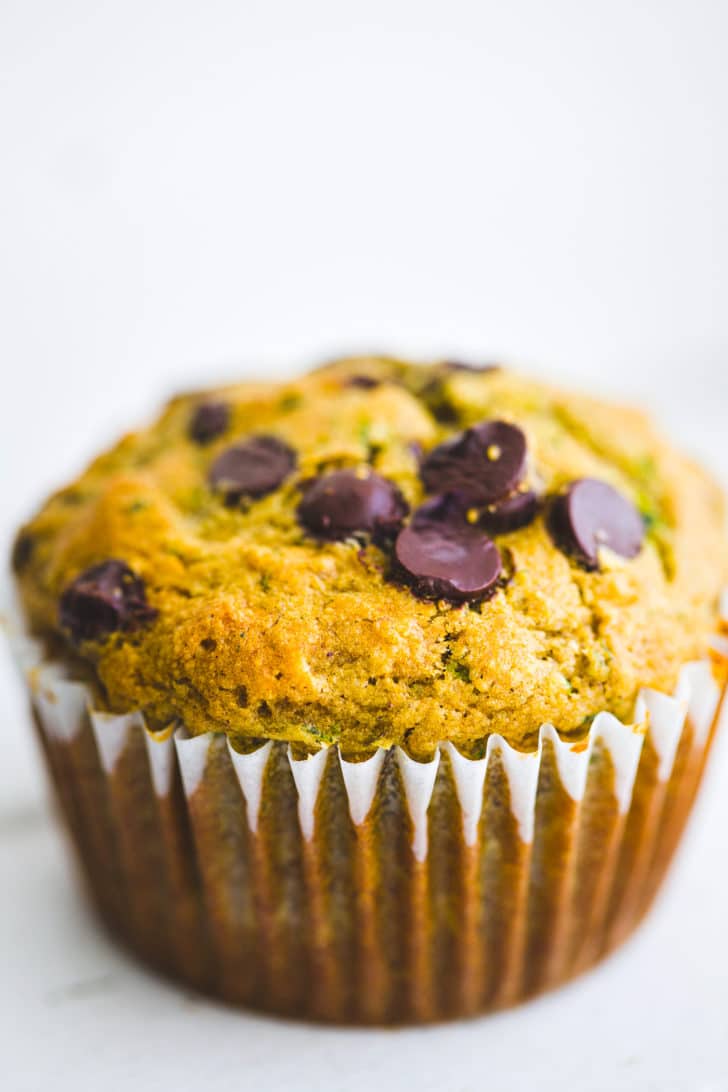 a close up image of a dairy free gluten free zucchini muffin with chocolate chips in a white muffin liner
