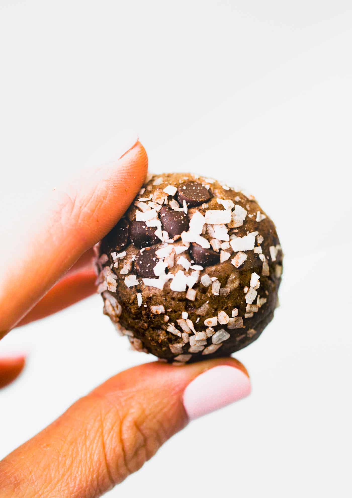 two fingers holding a coconut chocolate protein ball