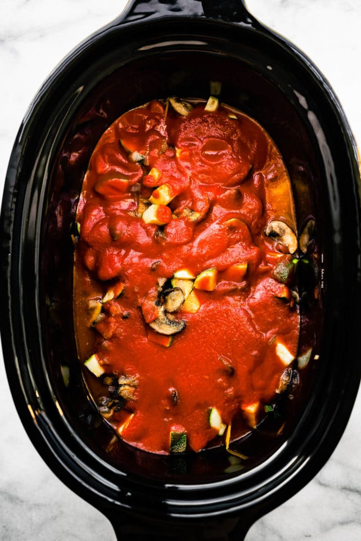 slow cooker full of tomato sauce, gluten free spaghetti noodles, chopped zucchini and mushrooms, and more tomato sauce