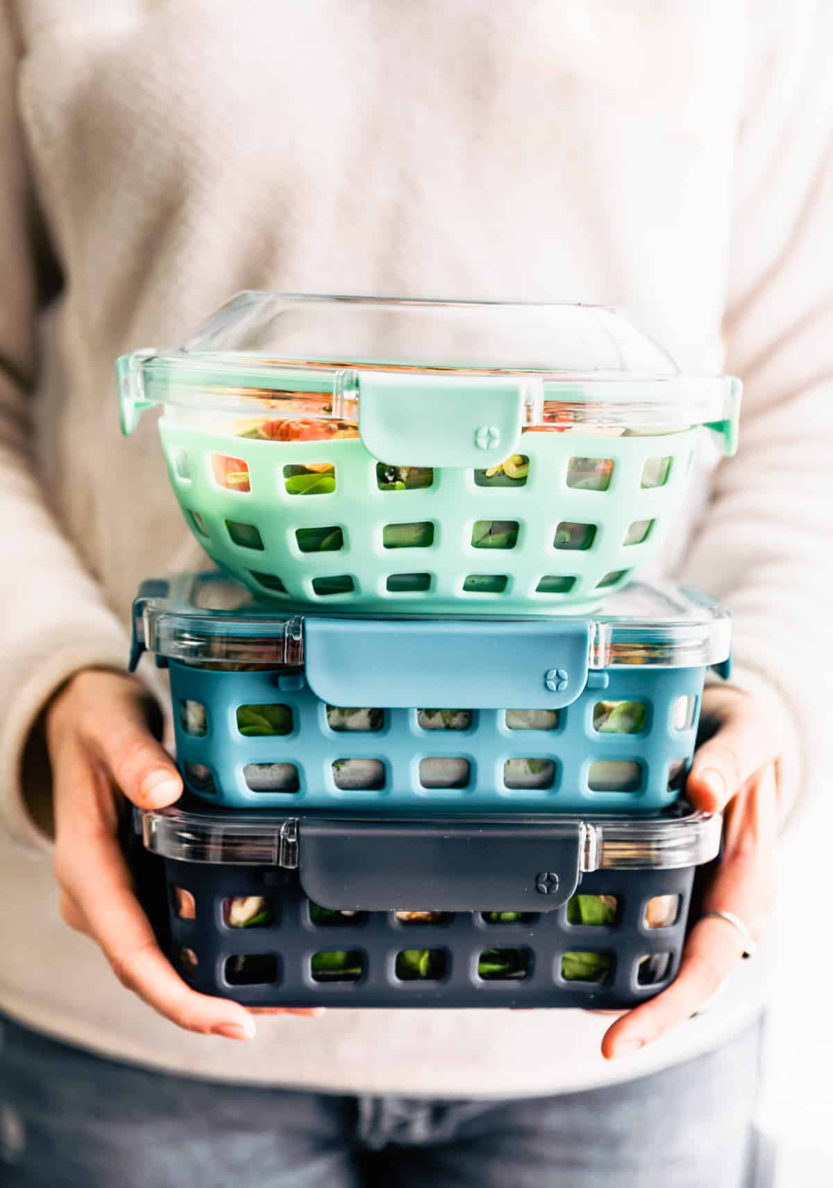 a woman holding a stack of three Ello containers full of food for meal prep