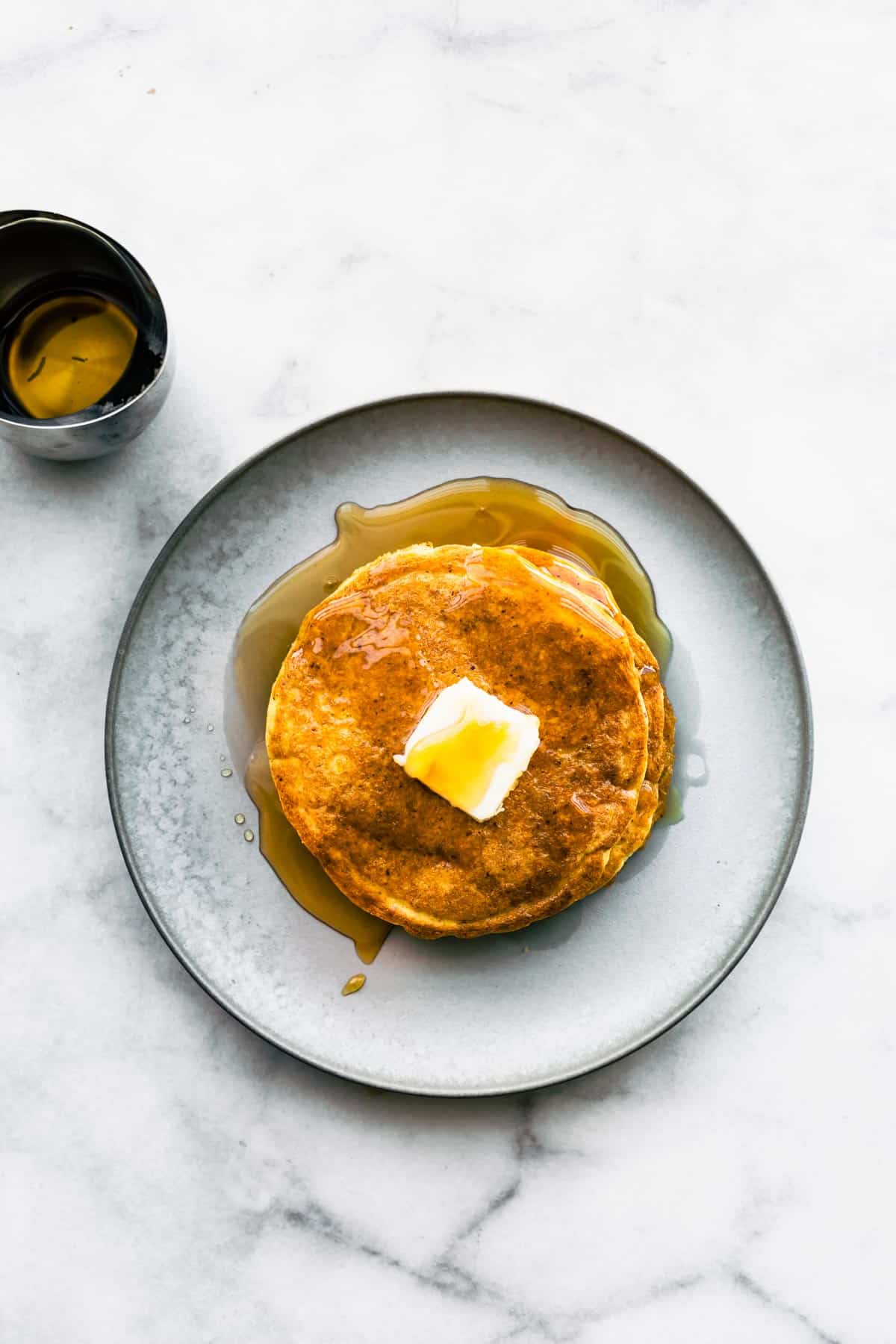 overhead image of a white plate with a stack of coconut flour pancakes topped with a pad of butter and maple syrup