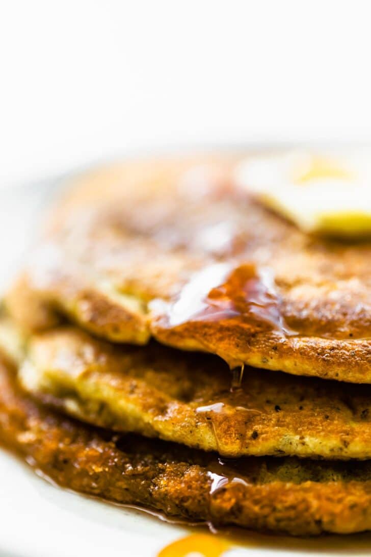 close up image of a stack of 3 coconut flour pancakes topped with butter and maple syrup