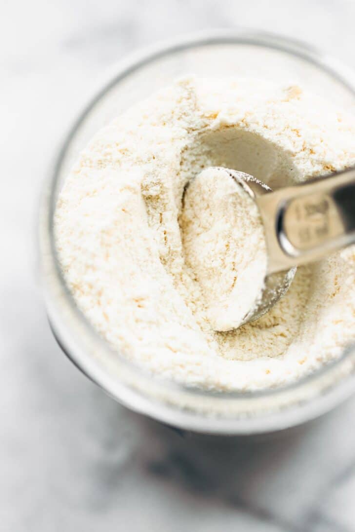 overhead image of a glass jar of gluten free flour with a measuring cup sticking out