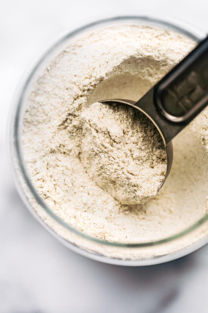 overhead image of a glass jar of gluten free oat flour with a measuring cup sticking out