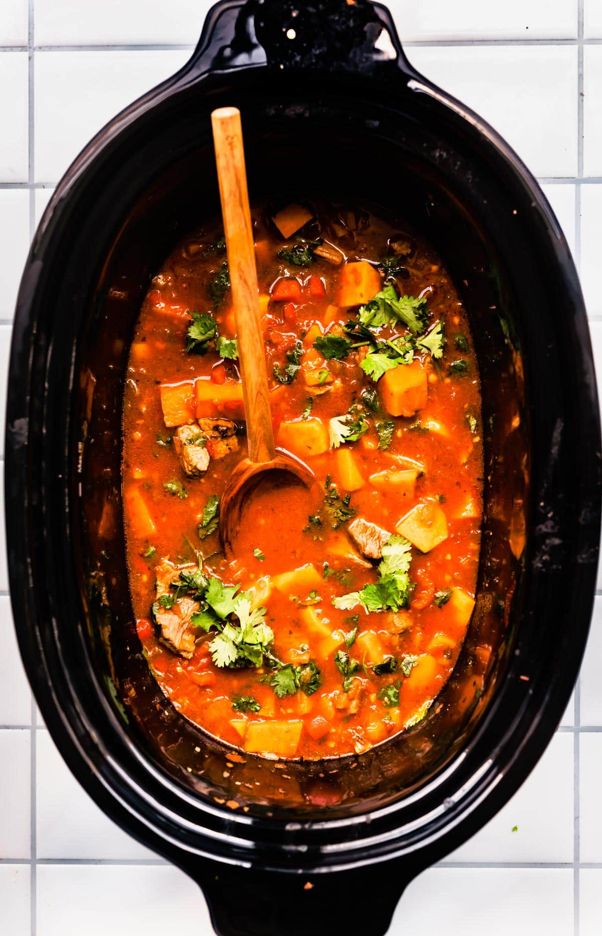 Overhead image of Mexican sweet potato beef stew in a slow cooker topped with fresh cilantro with a wooden spoon sticking out