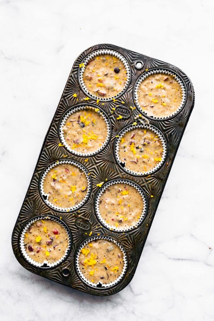 overhead image of a muffin tin full of gluten free cranberry orange muffins ready to be baked