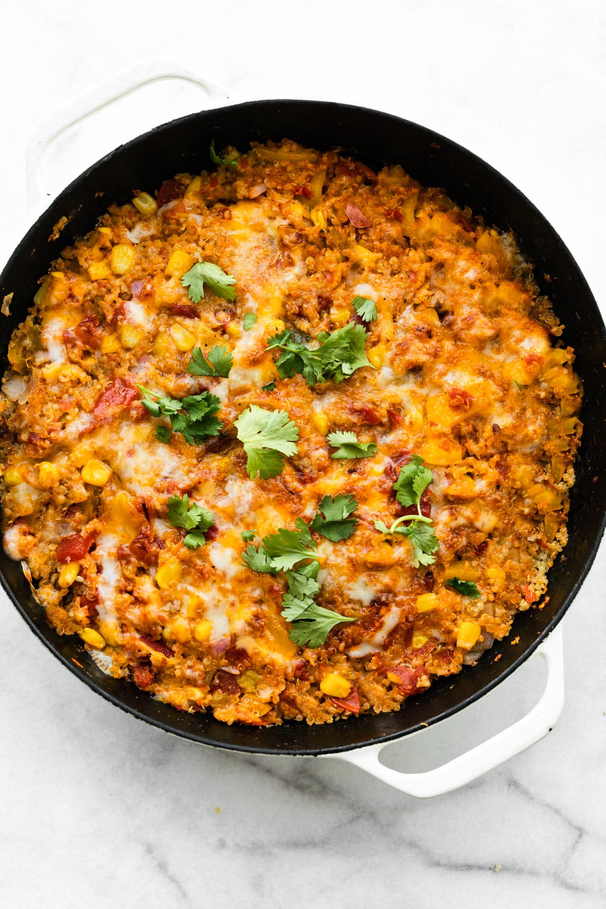 overhead image of one skillet mexican quinoa with melted cheese topped with fresh herbs