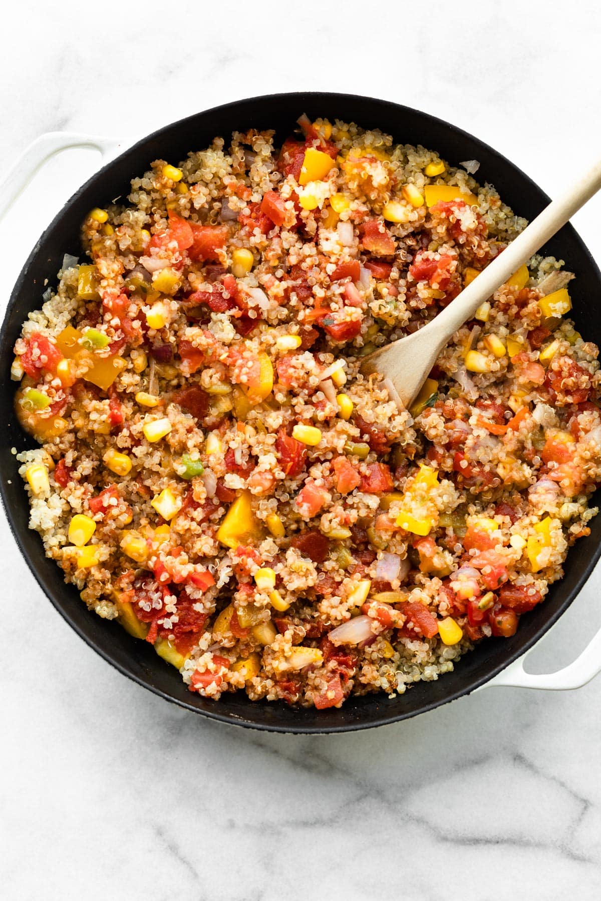 a skillet with mexican quinoa with a wooden spoon sticking out