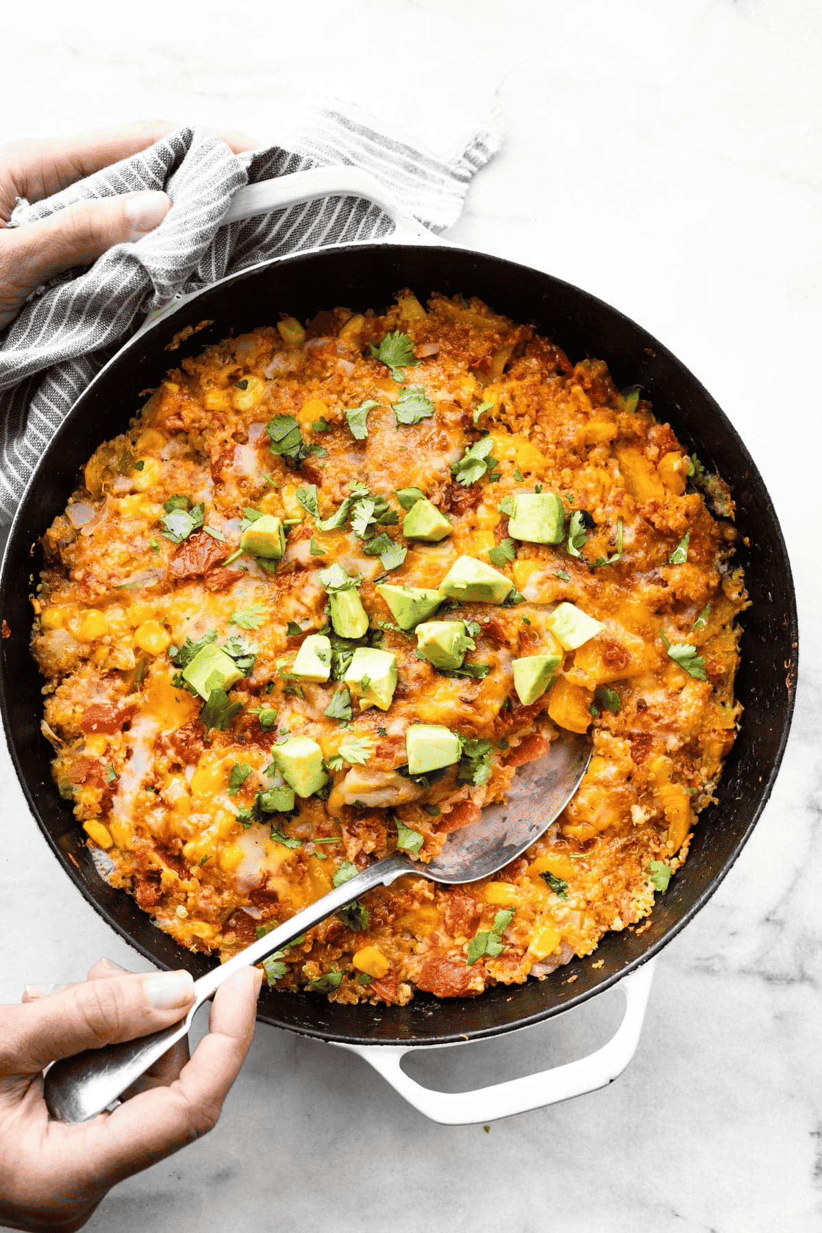 overhead image of one skillet mexican quinoa skillet toped with avocado with a hand dipping a spoon in the cneter