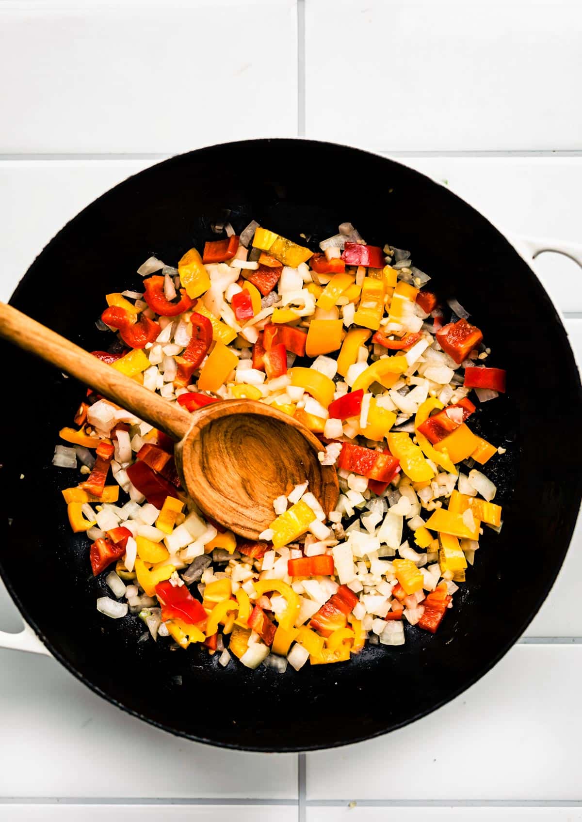 chopped onions and peppers in a skillet being stirred with a wooden spoon