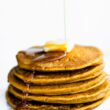 vegan pumpkin pancakes topped with dairy-free butter with maple syrup being drizzled on top