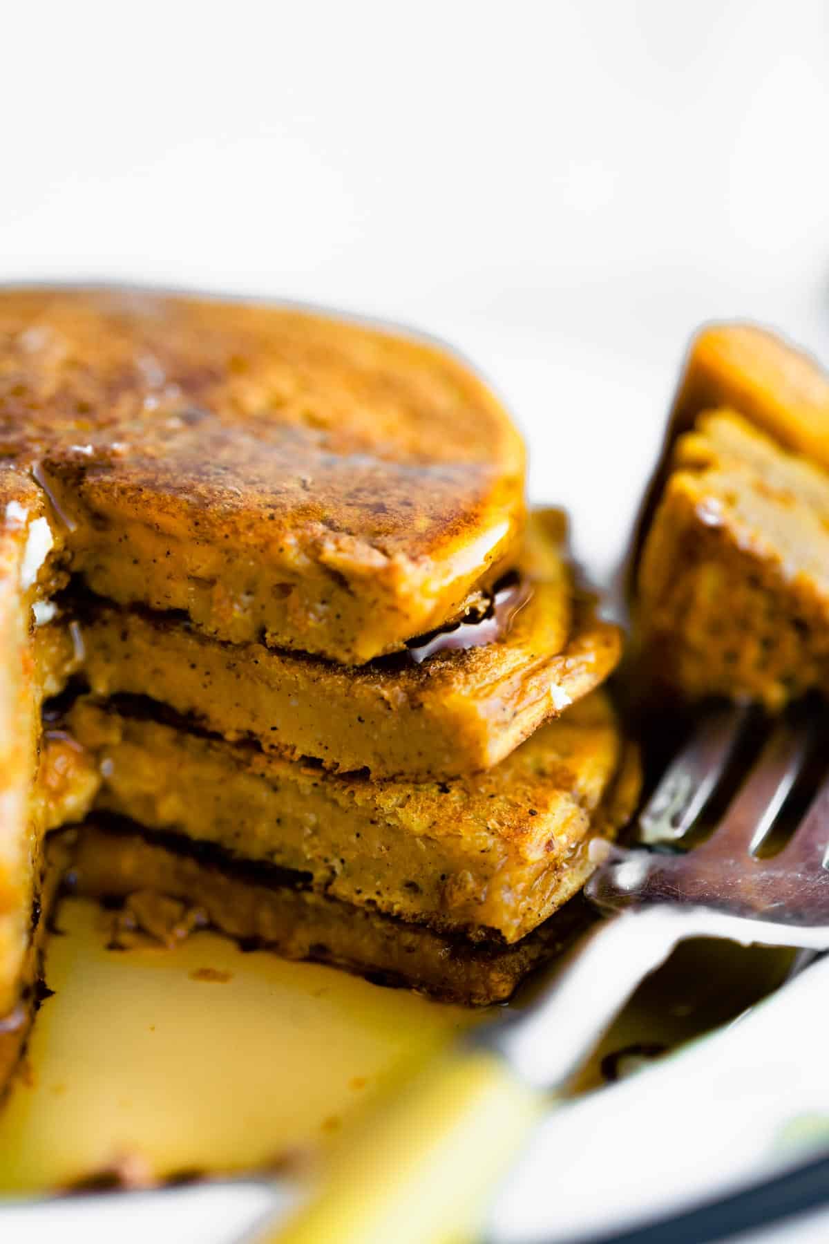 a stack of four vegan pumpkin pancakes with a fork full of pancakes topped with syrup