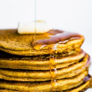 a stack of vegan pumpkin pancakes topped with a pad of butter being drizzled with maple syrup