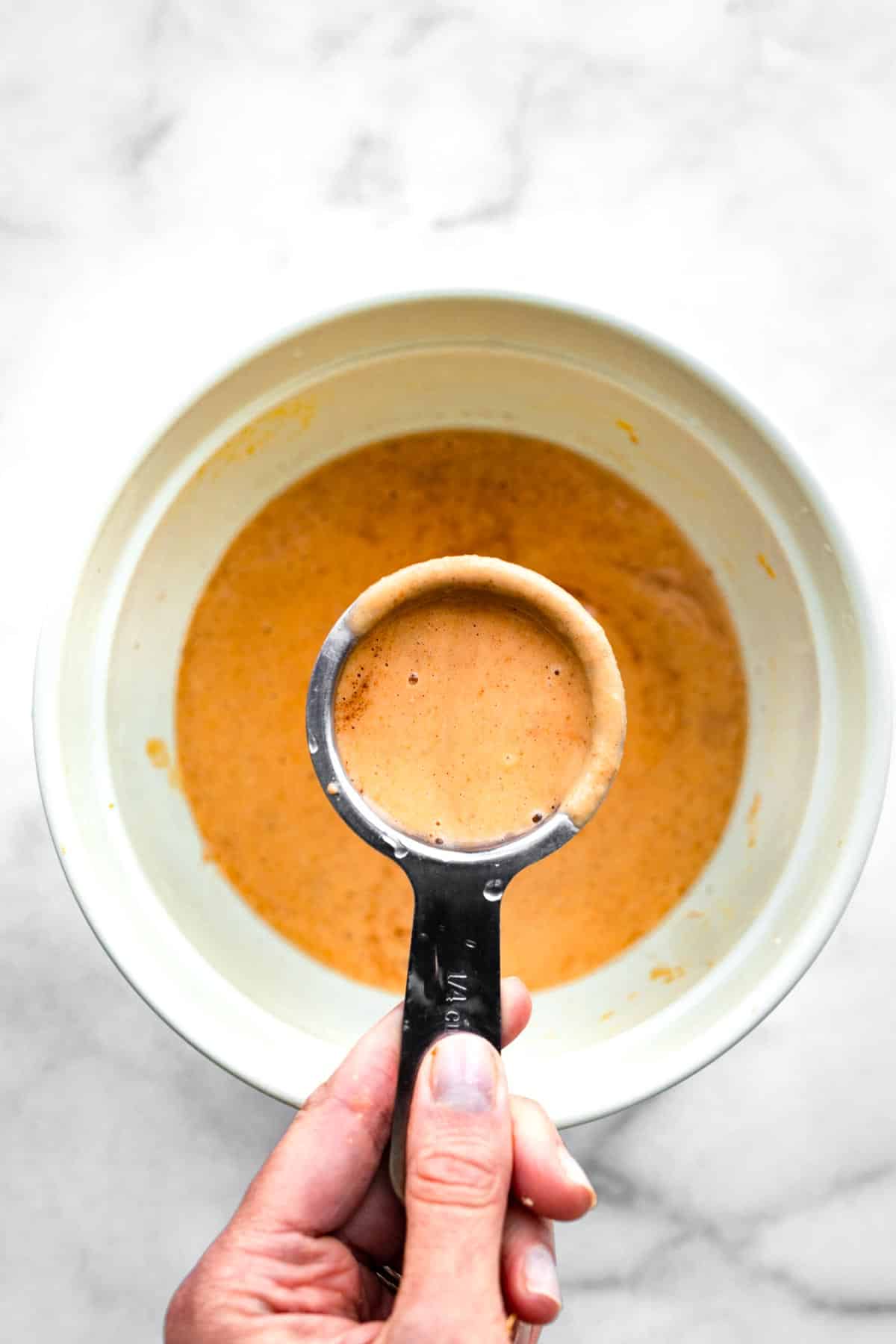 overhead image of a bowl of pumpkin batter being scooped up with a ¼ cup measuring cup