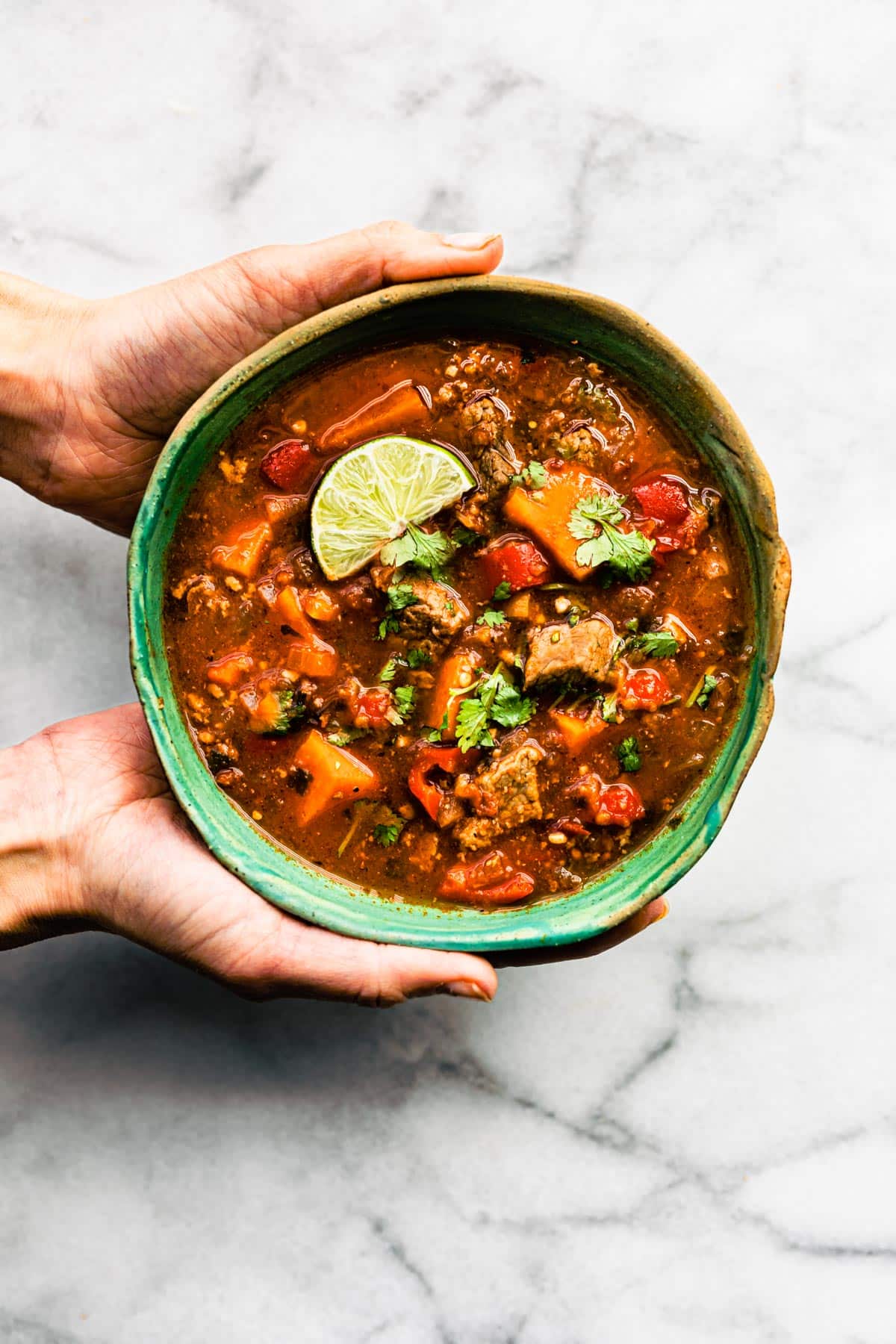 two hands holding a bowl of gluten-free Mexican sweet potato beef stew (slow cooker recipe)
