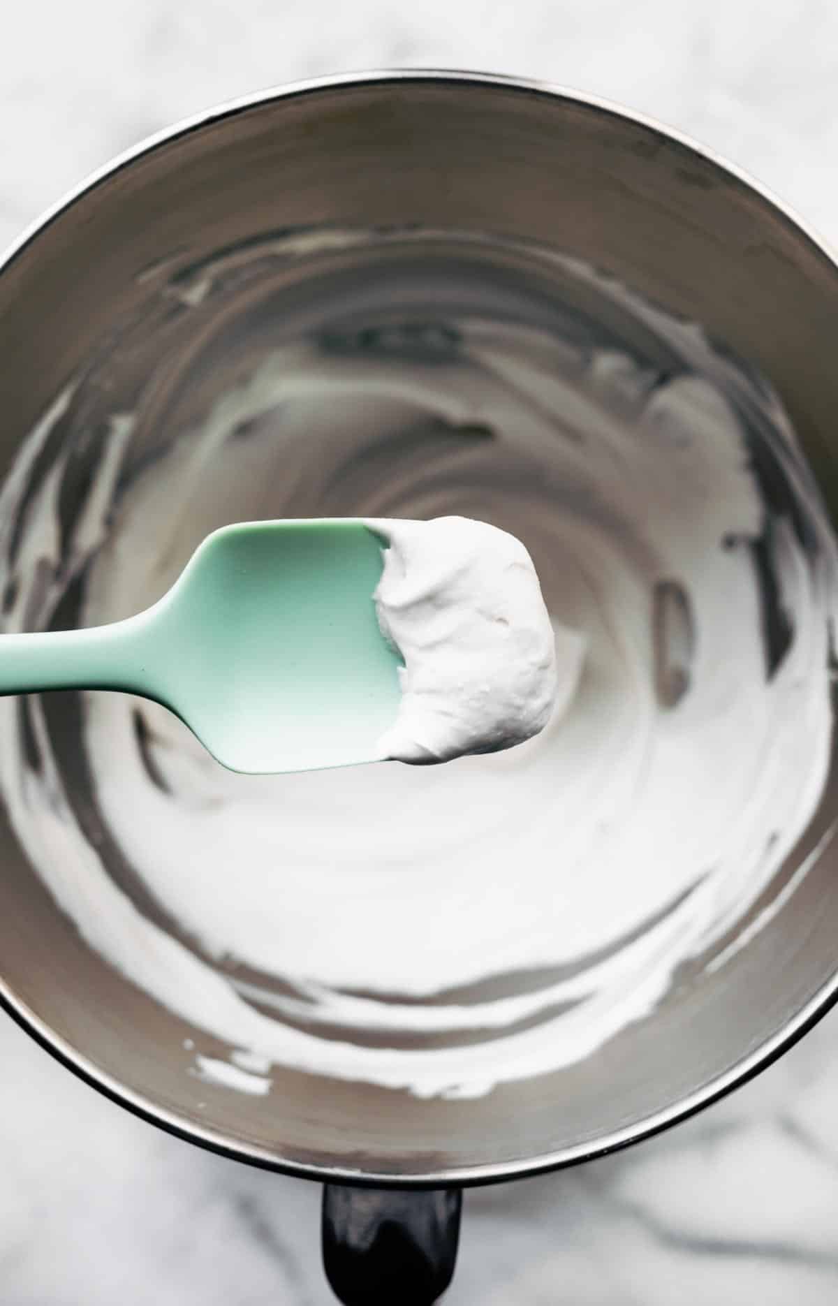 coconut cream frosting in a large mixing bowl with a spatula holding a dollop