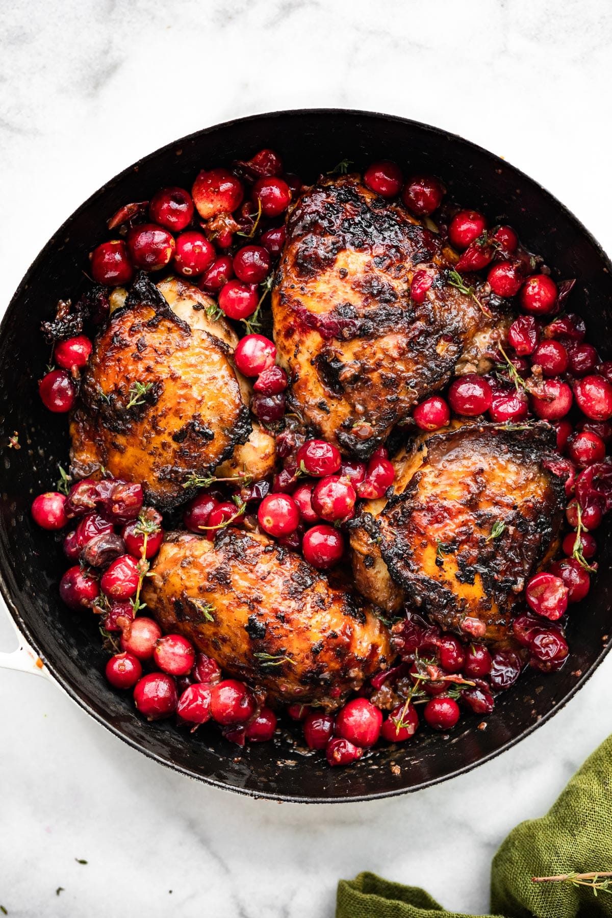 a skillet full of four balsamic roasted cranberry chicken thighs surrounded by roasted cranberries