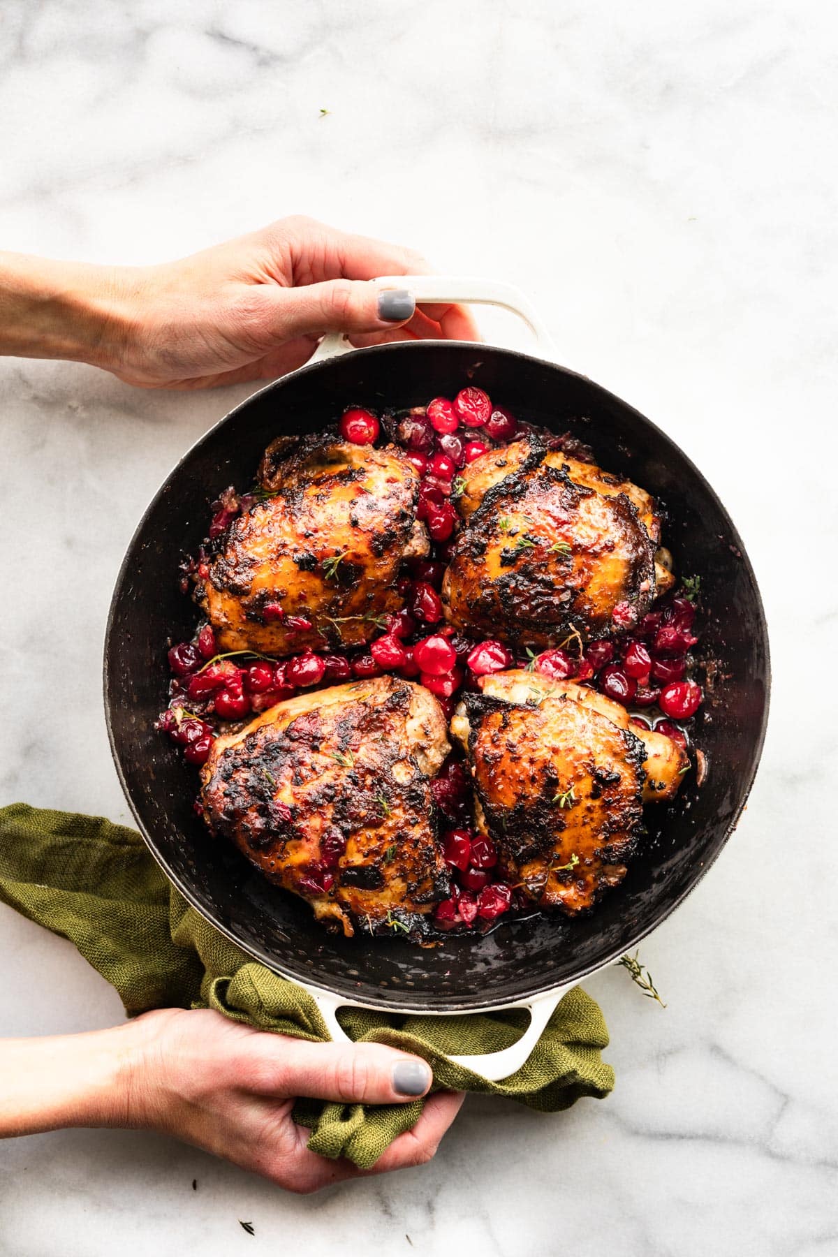 two hands holding a pot of balsamic roasted cranberry chicken thighs