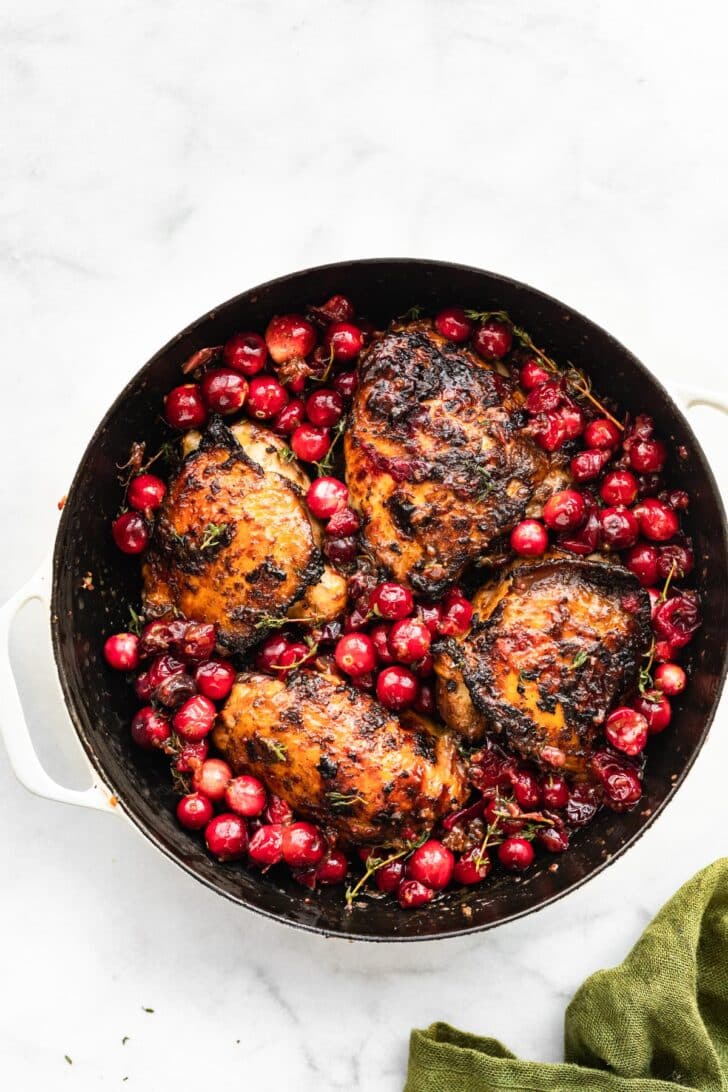 overhead image of a pot full of 4 balsamic roasted cranberry chicken thighs and roasted cranberries.