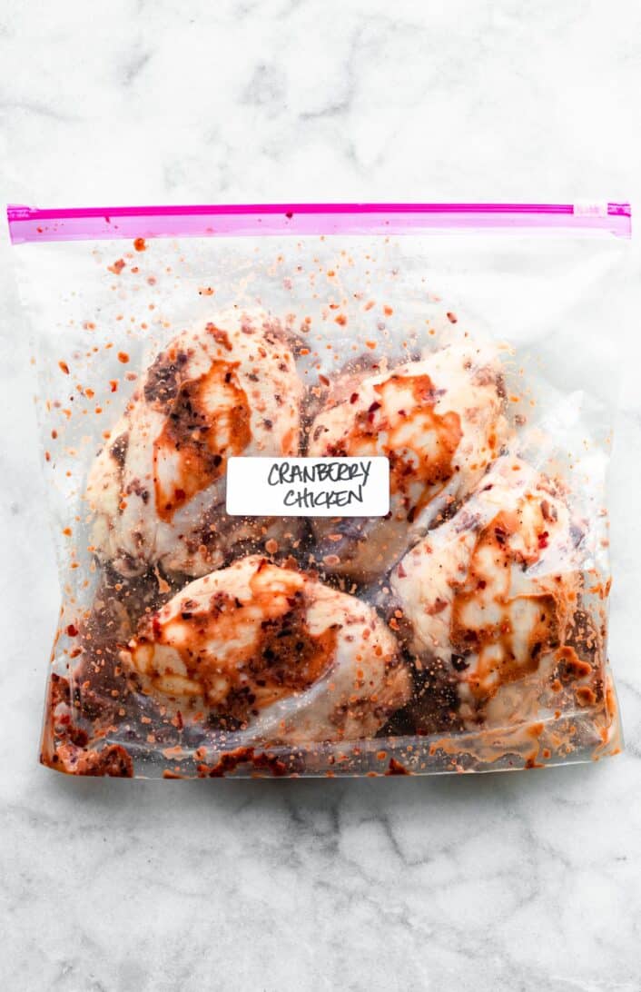 a ziploc bag labeled cranberry chicken full of four pieces of skin-on chicken in a marinade