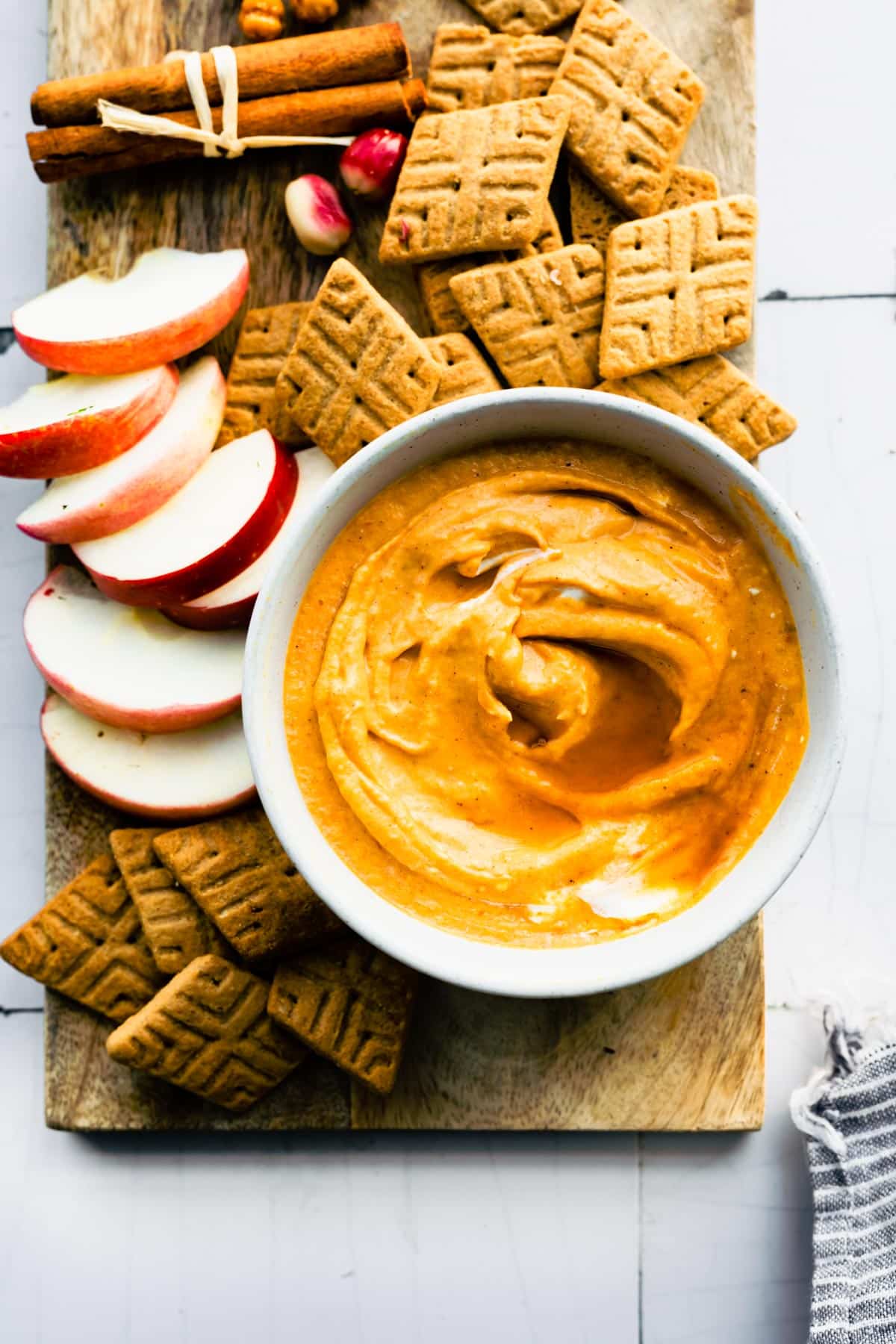 overhead image of a bowl of vegan pumpkin dip on a board surrounded by gluten free crackers and apple slices