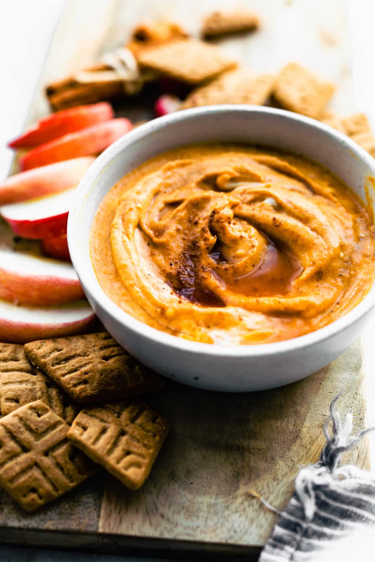 a bowl of vegan pumpkin dip with apples and gluten free crackers around