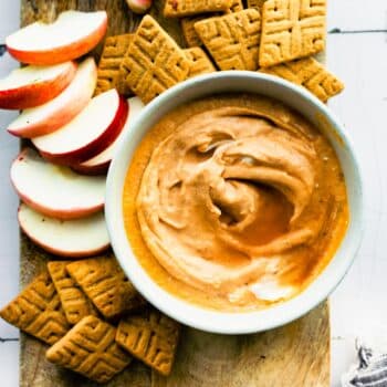overhead image of a bowl of vegan pumpkin dip on a board surrounded by gluten free crackers and apple slices